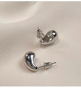 Vue macro de boucles d'oreilles goutte argentées avec finition miroir polie sur tissu doux
