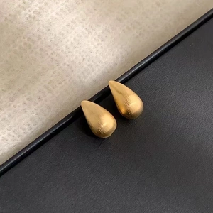 Gros plan de boucles d'oreilles goutte dorées avec texture en métal brossé sur noir