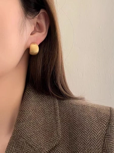 Nahaufnahme der mattgoldenen Ohrringe, getragen zu einem klassischen Fischgrät-Blazer