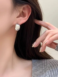 Macro side view of polished silver bean-shaped stud earrings on a female model ear