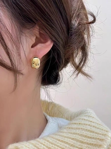 Macro view of gold rectangular stud earrings with polished metallic finish on a model