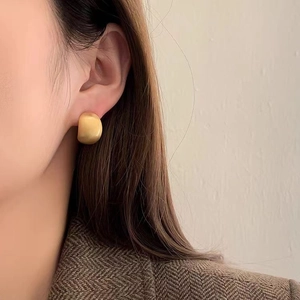 Minimalistische gebürstete goldene Ohrstecker in Halbzylinderform am Modell