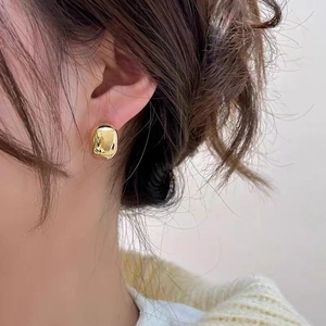 Minimalist glossy gold bean stud earrings shown on model with heavy metal texture