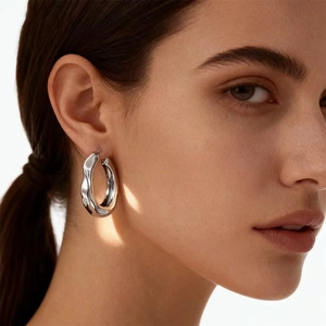 Nahaufnahme von minimalistischen, unregelmäßig strukturierten Creolen am Model mit Metallfinish