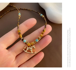 Detail of beaded necklace with gold rocking horse pendant and tiger eye stones