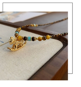 Close-up of golden rocking horse pendant with tiger eye beads and turquoise accents