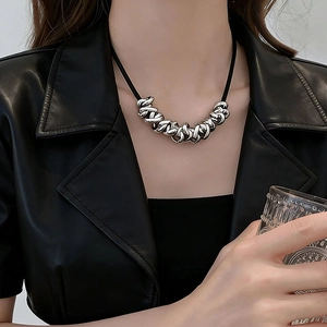 Close-up of irregular silver twisted metal rings on a black cord necklace worn by a model