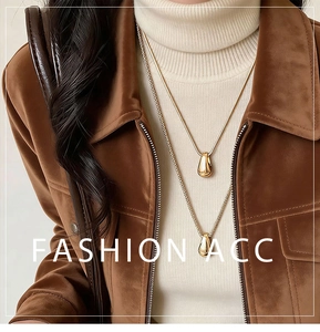 Detail of layered gold teardrop pendants on snake and rope chains over a white sweater