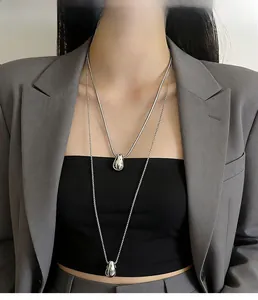 Close-up of layered silver teardrop necklace with snake chain on a model in a gray suit
