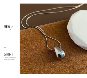 Close-up of polished silver teardrop pendant with a sleek snake chain on a textured base