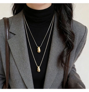 Detail of layered gold teardrop necklace on model with chic minimalist aesthetic