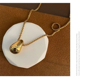 Close-up of a minimalist golden waterdrop pendant with a polished mirror finish on a box chain
