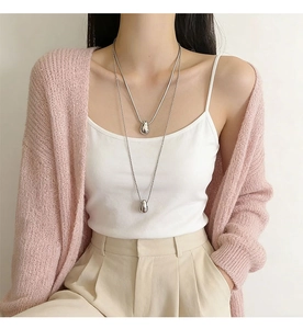 Detailed view of layered silver teardrop necklaces worn over a pink knit sweater