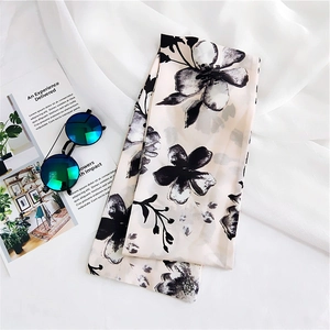 Close-up of narrow silk scarf with black floral print on cream fabric and sunglasses