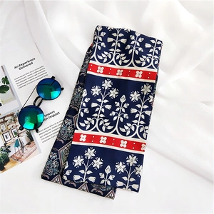 Floral navy silk scarf with red borders laid by blue sunglasses and a magazine