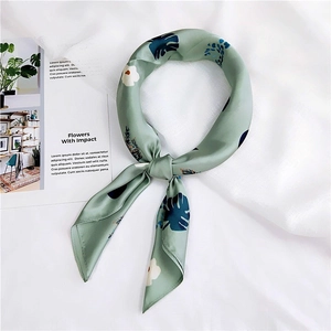 Detailed close-up of light green silk scarf with blue leaf pattern on white fabric