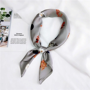 Satin neck scarf with gray base, vibrant floral patterns and blue dots in a knotted style