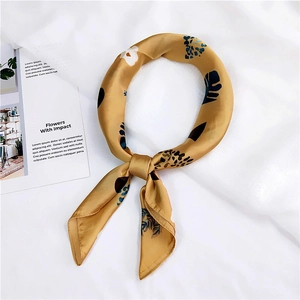 Elegant gold silk scarf with blue leaf pattern knotted on a clean white fabric backdrop