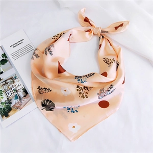 Close-up of beige silk square scarf with leaf print tied in a bow on white fabric