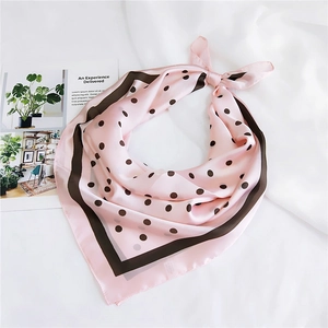 Foulard en soie rose à pois avec bordure marron, plié sur un fond en tissu doux