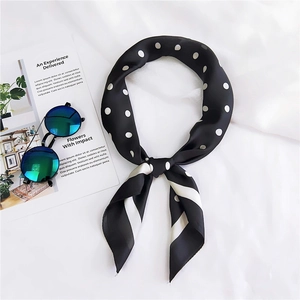 Gros plan d'un foulard en soie noir à pois blancs et bordure rayée sur fond blanc