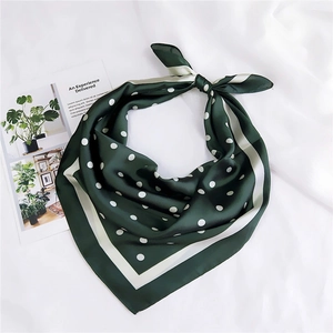 Détail d'un foulard en soie vert foncé à pois blancs posé sur un tissu blanc texturé