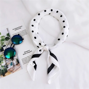 Gros plan d'un foulard en soie blanc à pois noirs et bord rayé sur un fond en tissu blanc