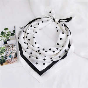 Gros plan d'un foulard en soie à pois noir et blanc noué sur tissu blanc