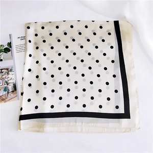 Détail d'un foulard en soie à pois avec bordure noire sur fond en tissu crème