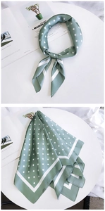 Détail du foulard en soie vert sauge à pois drapé sur un support blanc minimaliste