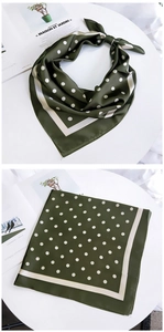 Détail d'un foulard en soie vert foncé à pois, présenté à plat et noué sur table