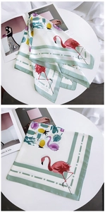 Detail of square silk scarf with flamingo and pineapple print on a white table