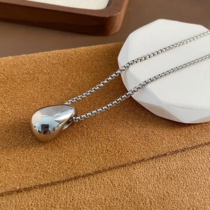 Minimalist silver water drop pendant necklace with a polished box chain on a premium stand