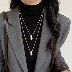Minimalist double-layered gold necklace with teardrop pendant on chic grey blazer