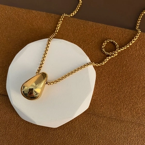 Minimalist gold teardrop pendant necklace with high-polished finish on white pedestal