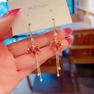 Detailed macro shot of red crystal maple leaf earrings with elegant gold fringe tassels