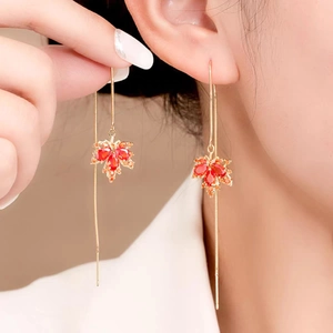 Close-up of red crystal maple leaf earrings with long golden fringe tassels on a model