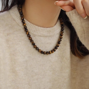 Collier en perles d'œil de tigre avec texture lustrée sur un pull en maille beige