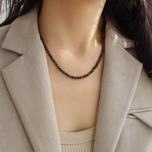 Gros plan d'un collier de perles en oeil de tigre porté sur une tenue élégante