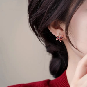 Elegant maple leaf earrings with red crystals and gold finish on a female model