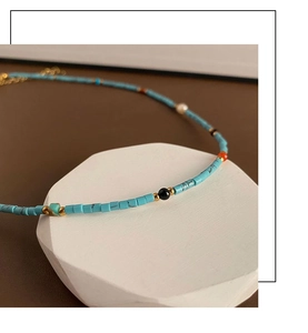 Macro shot of turquoise beaded necklace with gold accents and a white pearl detail