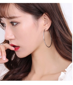 Détail macro d'une grande boucle d'oreille créole argentée portée par un mannequin