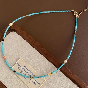Beaded necklace with turquoise squares, white pearls, and gold clasp in a wooden tray