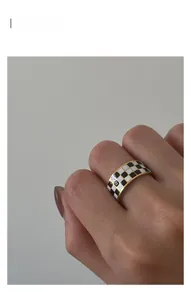 Detailed view of checkered gold ring band with black and white pattern on finger