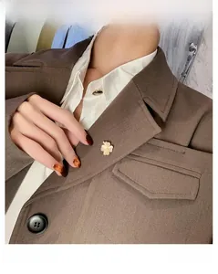 Vue détaillée d'une broche trèfle avec pétales en nacre sur une veste de costume marron