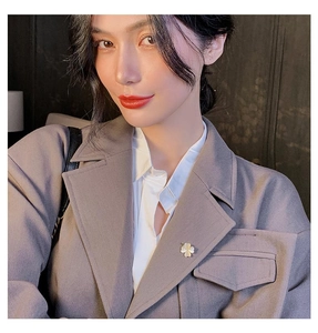 Détail d'une broche trèfle en nacre blanche sur le revers d'un tailleur gris chic
