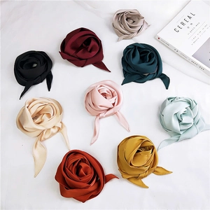 Detail of nine colorful satin neck scarves folded into elegant rose shapes on white fabric
