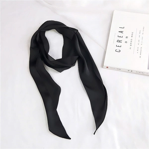 Flat lay of a black satin skinny scarf with a magazine on a white fabric background