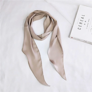 Detail shot of a champagne silk skinny scarf on a minimalist linen background