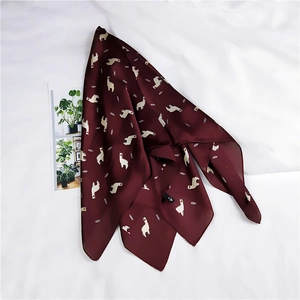 Détail d'un foulard en soie bordeaux avec imprimé alpaga et plumes sur tissu blanc